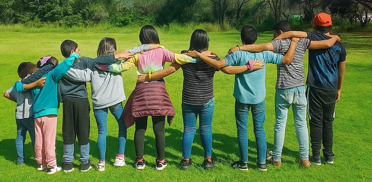 Niños y adolescentes con los brazos sobre los hombros en un espacio al aire libre