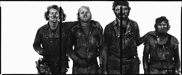 Retrato en blanco y negro de cuatro trabajadores con la ropa y el rostro manchados, de pie frente a un fondo blanco, perteneciente a la serie In the American West de Richard Avedon.