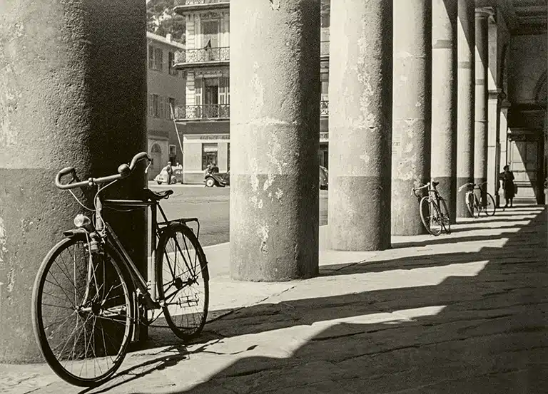 Bicycle leaning against a stone column beneath a porticoed gallery.