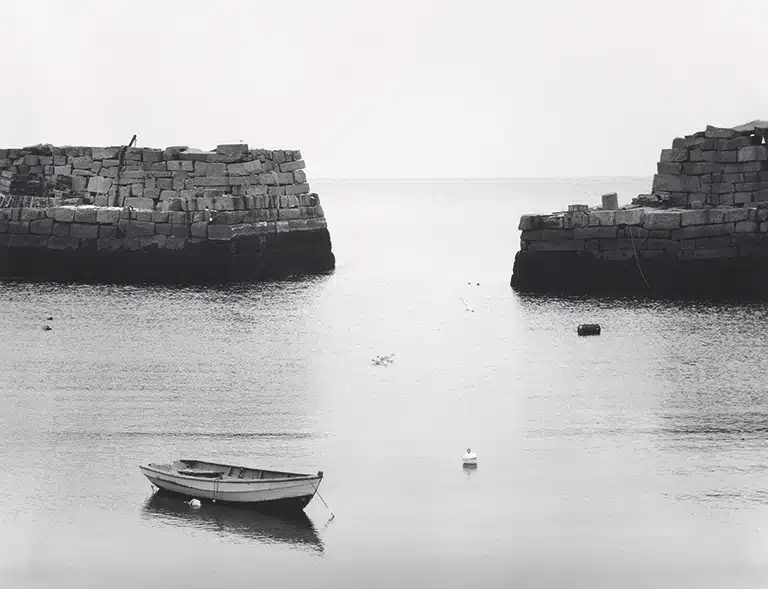 Boat on calm water between stone walls in black and white