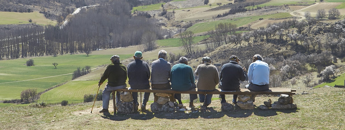 Personas mayores sentadas al aire libre en un entorno rural.