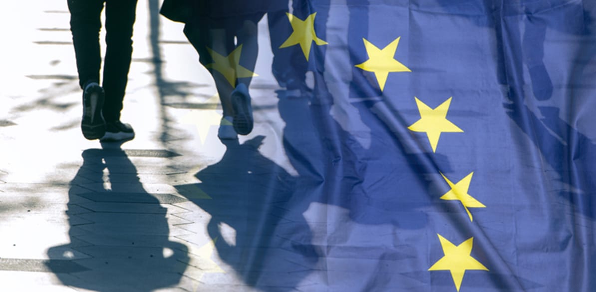 Personas caminando por la calle con superposición de la bandera de la Unión Europea en primer plano.