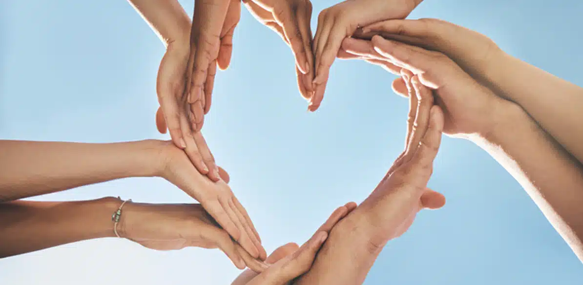 Manos de varias personas formando un corazón sobre fondo azul, símbolo de unión y colaboración.