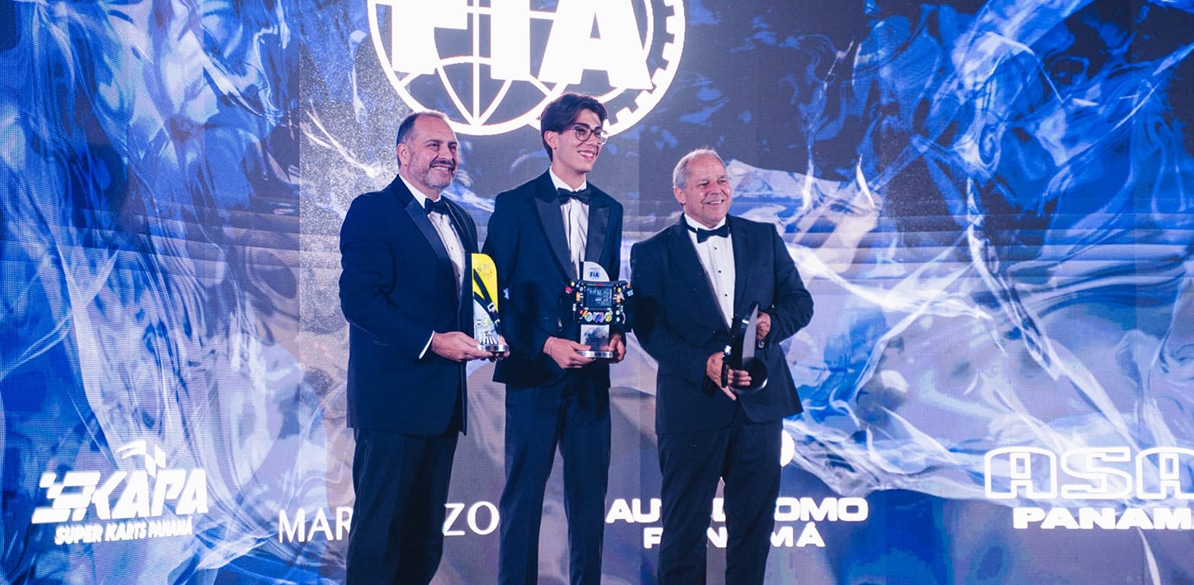 Tres personas, una con un trofeo y las otras dos sosteniendo premios de reconocimiento. Están de pie en un evento formal con fondo azul, mostrando un ambiente de celebración y éxito. La imagen refleja un evento relacionado con premios en el ámbito de la movilidad, donde se reconocen logros en seguridad vial.