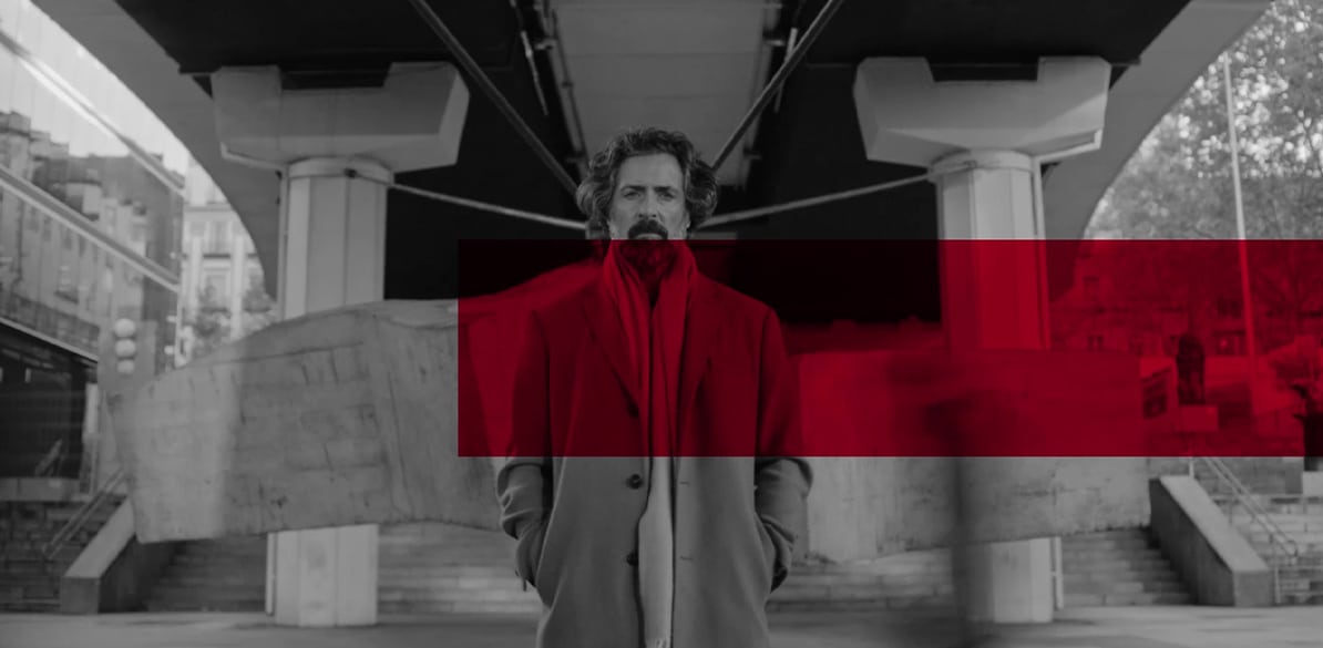 Hombre con abrigo rojo en blanco y negro frente a un edificio