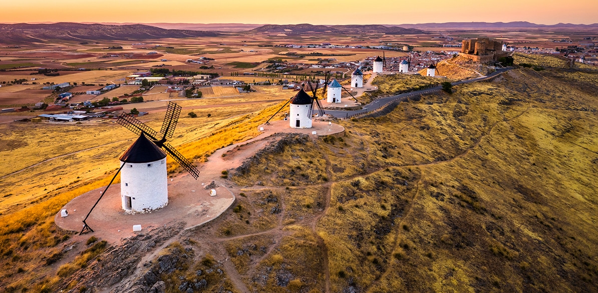 Vista aérea de los molinos de viento de Consuegra, un símbolo de la cultura española. La imagen representa la esencia del medio rural, reflejando el impulso de proyectos sociales como el programa Ayudas+Rural 2025 para mejorar la vida en estas zonas con 18 millones de euros.