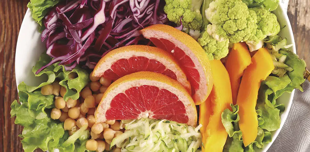 Bol de ensalada saludable con hojas de lechuga, garbanzos, col lombarda en tiras, rodajas de pomelo, ramilletes de coliflor, tiras de pimiento amarillo y verduras frescas.