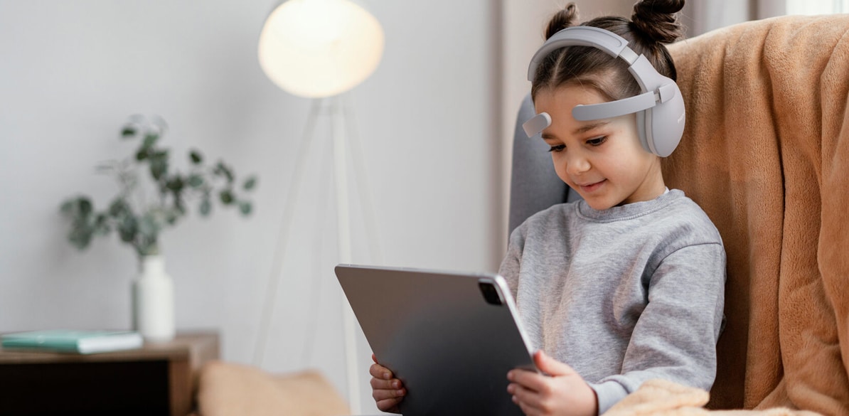 Niña con auriculares y casco EEG usando una tablet durante una sesión de neurofeedback