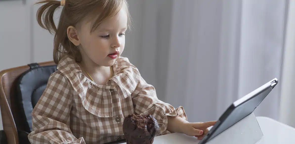 TDAH Niña utilizando una tableta mientras come una magdalena.