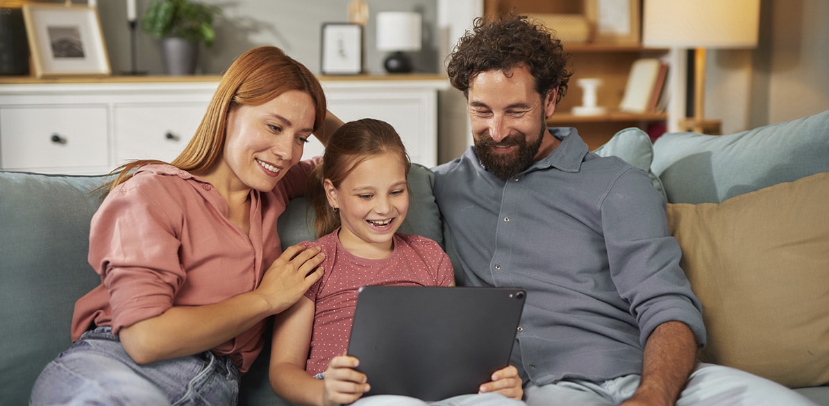 Guías Familia con una niña utilizando una tablet en el sofá de casa mientras comparten un momento juntos.