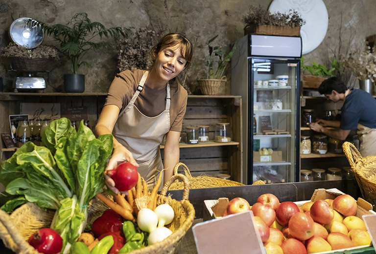 Asociación Cesal Woman in an organic produce store selecting fresh vegetables while a man organizes products in the background.