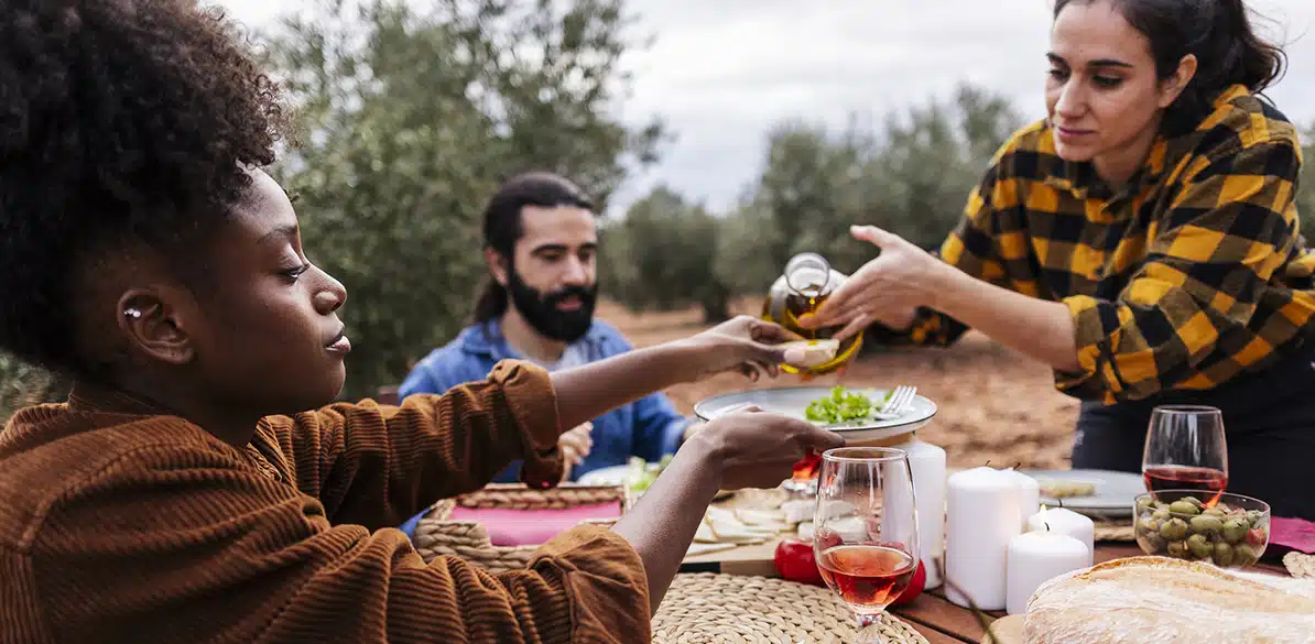 COCEMFE Group of people providing and sharing food outdoors in a rural setting, surrounded by fields and nature, promoting community.