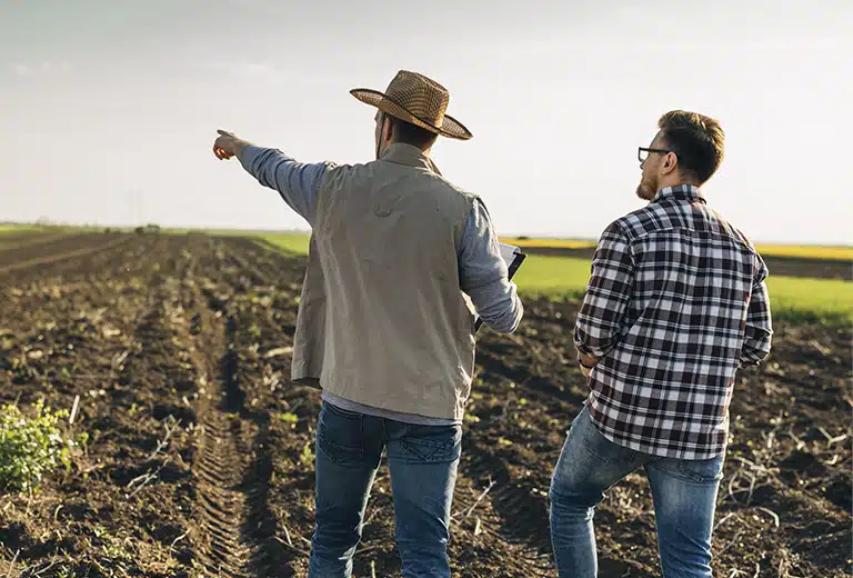 Male farmers inspecting a freshly plowed field at sunset, one pointing to the plot as they review the agricultural land for sustainable rural production planning and management.