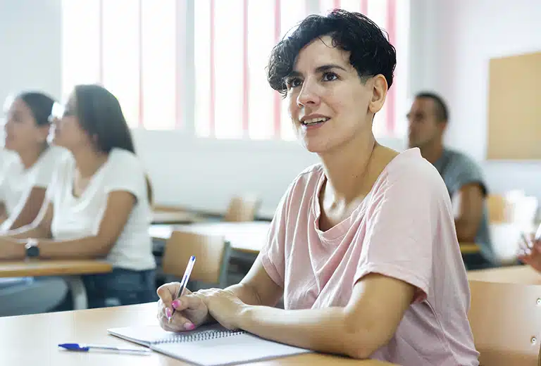 Fundación San Cebrian Woman with short hair sitting in a classroom, taking notes with a pen while attending a training session; other people out of focus in the background.