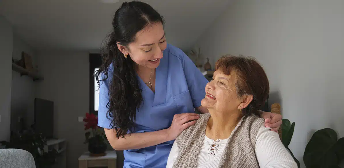 Fundación Valentia Huesca A caregiver or healthcare professional in a blue uniform accompanies and talks to an elderly woman sitting in her home, showing support and providing home care.