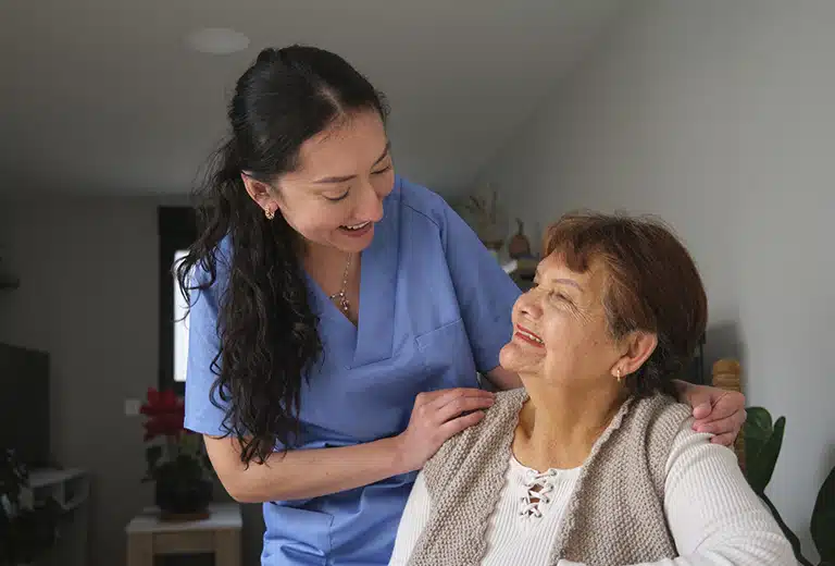 Fundación Valentia Huesca A caregiver or healthcare professional in a blue uniform accompanies and talks to an elderly woman sitting in her home, showing support and providing home care.