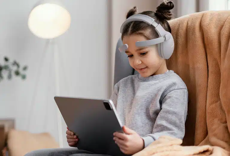 Niña con auriculares blancos usando una tableta sentada en un sillón en casa, representando la neurotecnología pediátrica del proyecto PigPug Health para niños con TDAH y autismo.