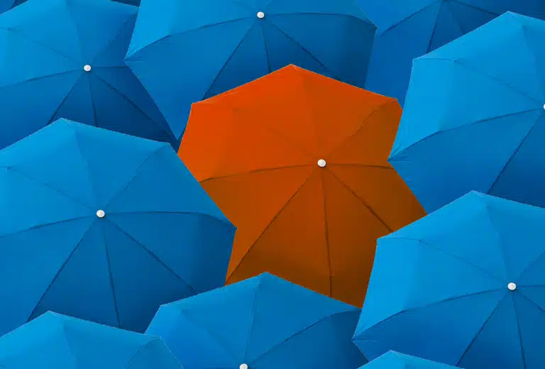 Ilustración de varios paraguas azules reodeando un paraguas naranja en el centro, creando contraste.